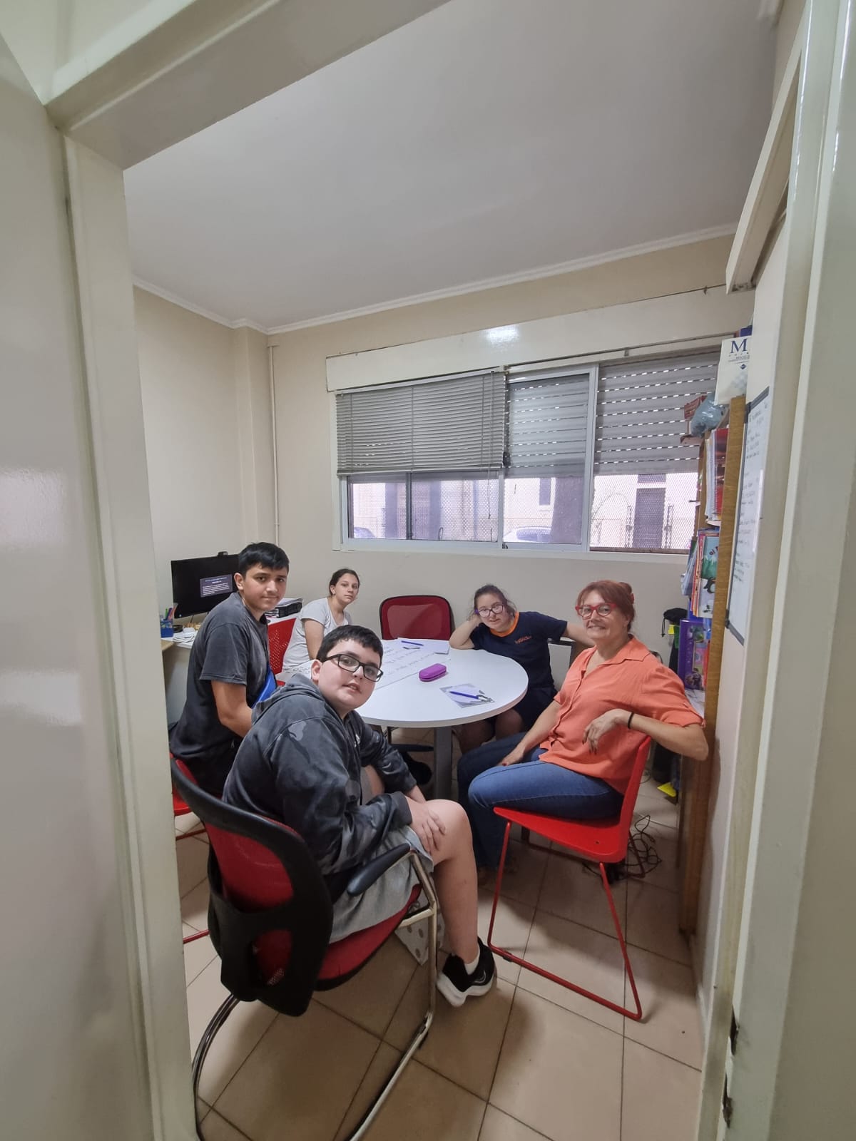 En la imagen se ve a un grupo de adolescentes sentados al rededor de una mesa redonda junto a la directora de la institución.